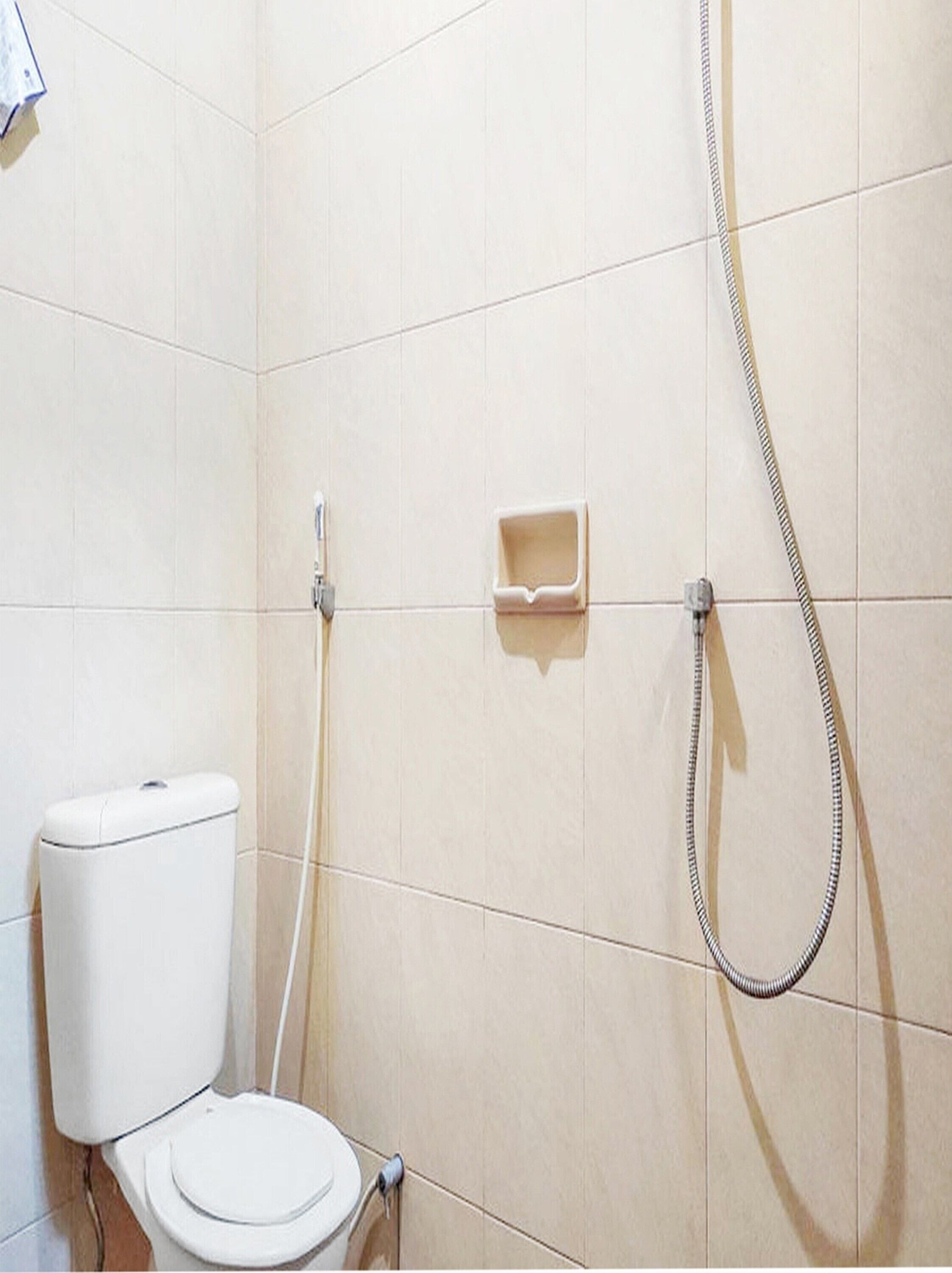 A small, tiled bathroom with a toilet, a handheld showerhead, and a soap dish.