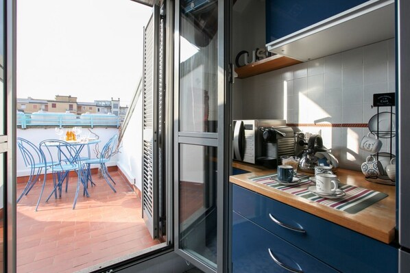 Una cocina moderna con un ventanal que da a un balcón con sillas azules y una mesa.