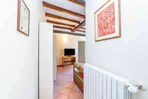 Ein Flur mit Holzboden, einem Heizkörper, einem Fernseher auf einem Standfuß und einem gerahmten Bild an der Wand.