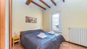 A bedroom with a bed, a window, a radiator, and a small table with a lamp. - GuestHost - Two-room apartment located on the second floor of a building, without lift, located in the heart of the historic center of Parma. The property enjoys a central location (ZTL), in a picturesque, popular and lively district, near the Don Gnocch (Parma)