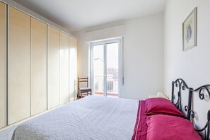 Un dormitorio con cama, armario, silla y puerta al balcón.