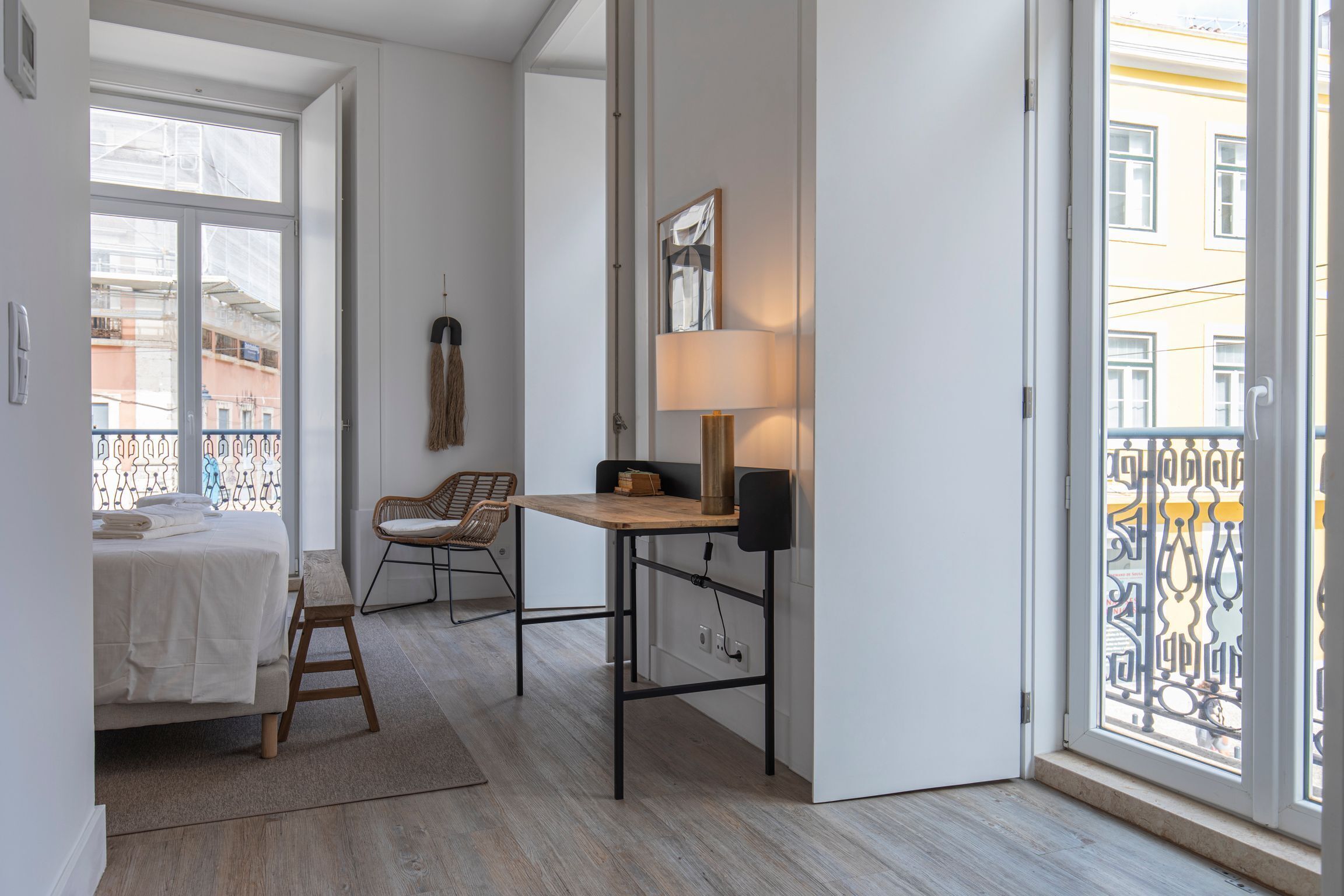 Une chambre à coucher de taille modeste, comprenant un lit, une petite table en bois, une chaise et une fenêtre donnant sur des immeubles.