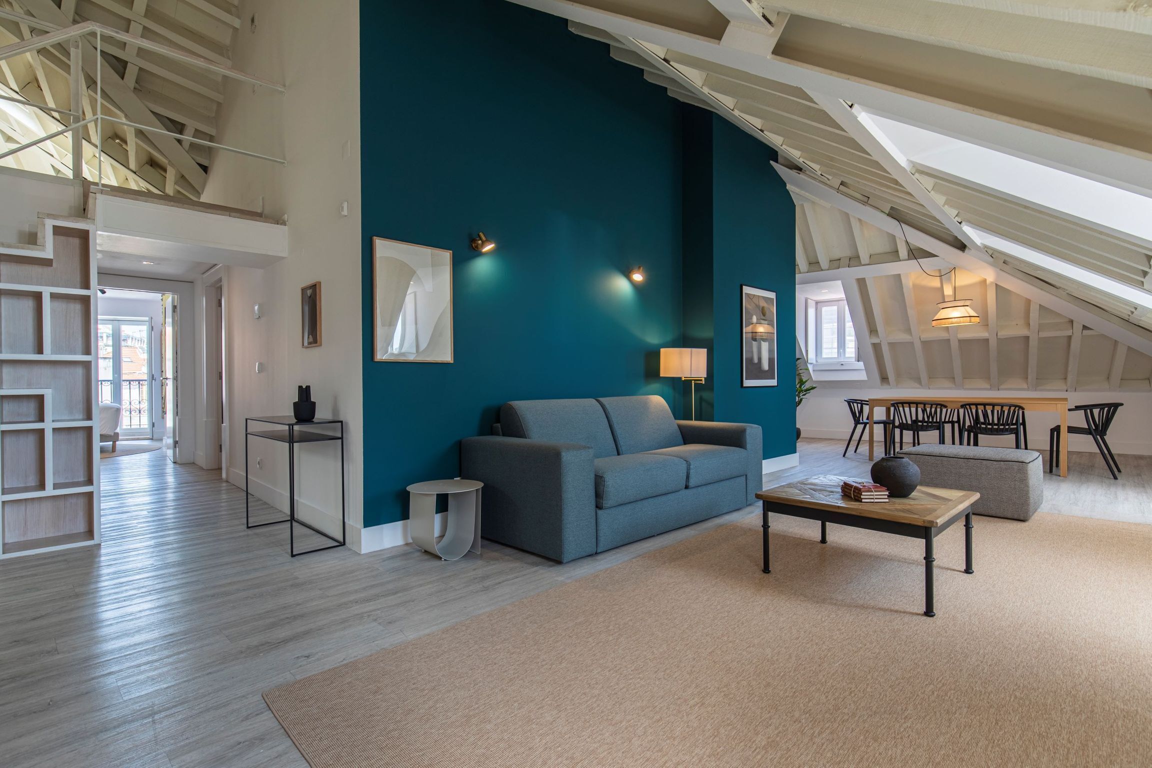 A modern living room with a teal accent wall, a sofa, a coffee table, and a dining area with chairs.