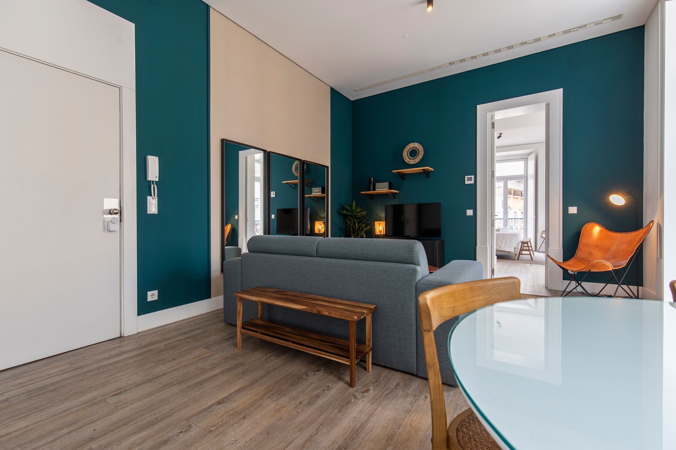 En moderne stue med teal vægge, en grå sofa, et træ sofabord og et glas spisebord.