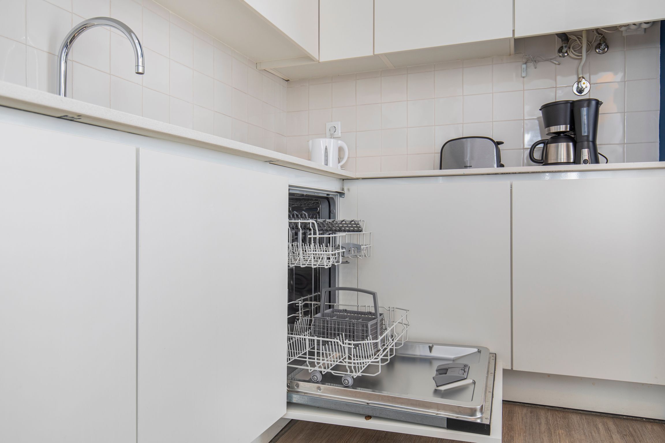 Une cuisine moderne avec des meubles blancs, un lave-vaisselle, une machine à café et une bouilloire.