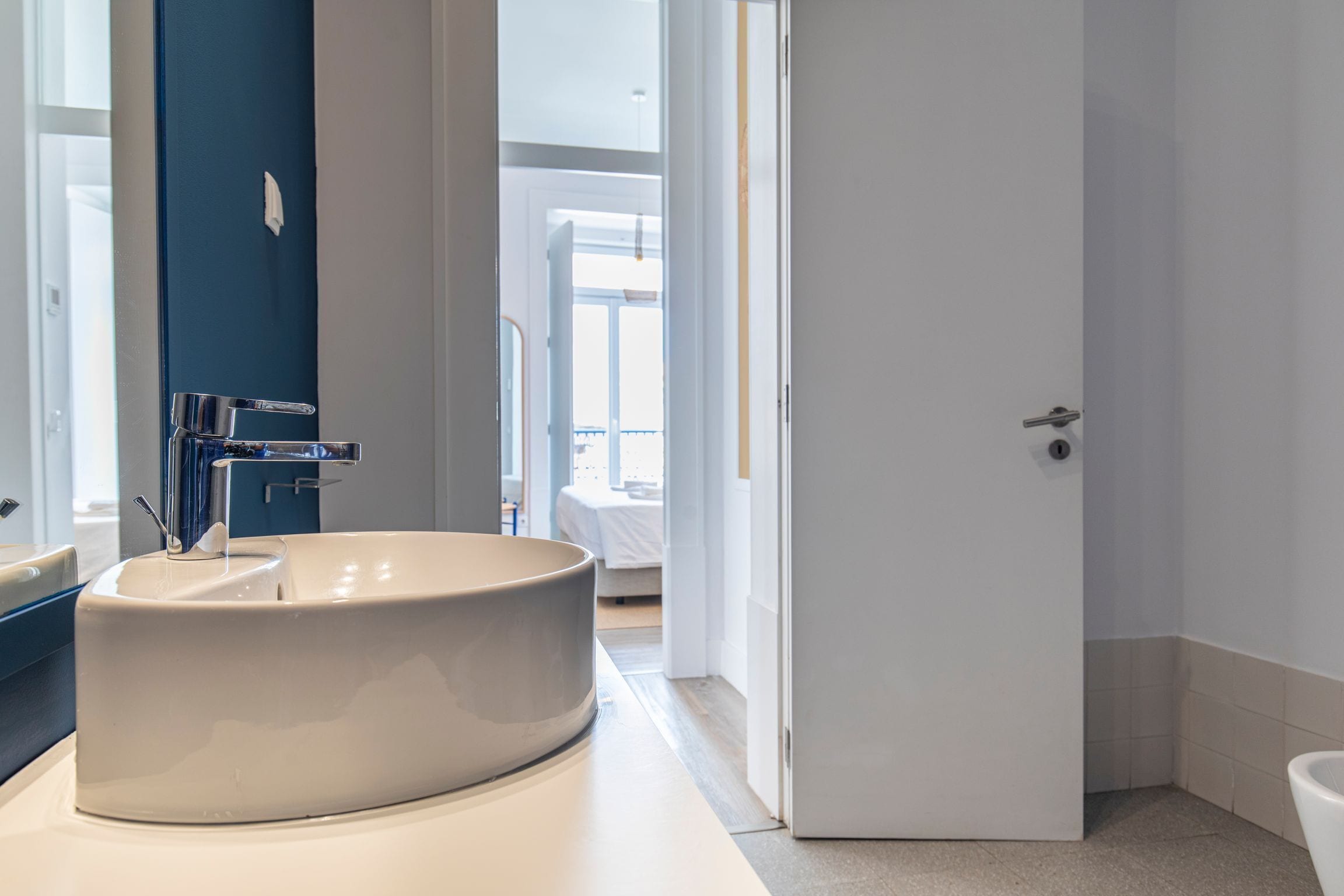 Ein modernes Badezimmer mit einem großen, runden Waschbecken, einem Spiegel und einer Tür zu einem weiteren Raum.