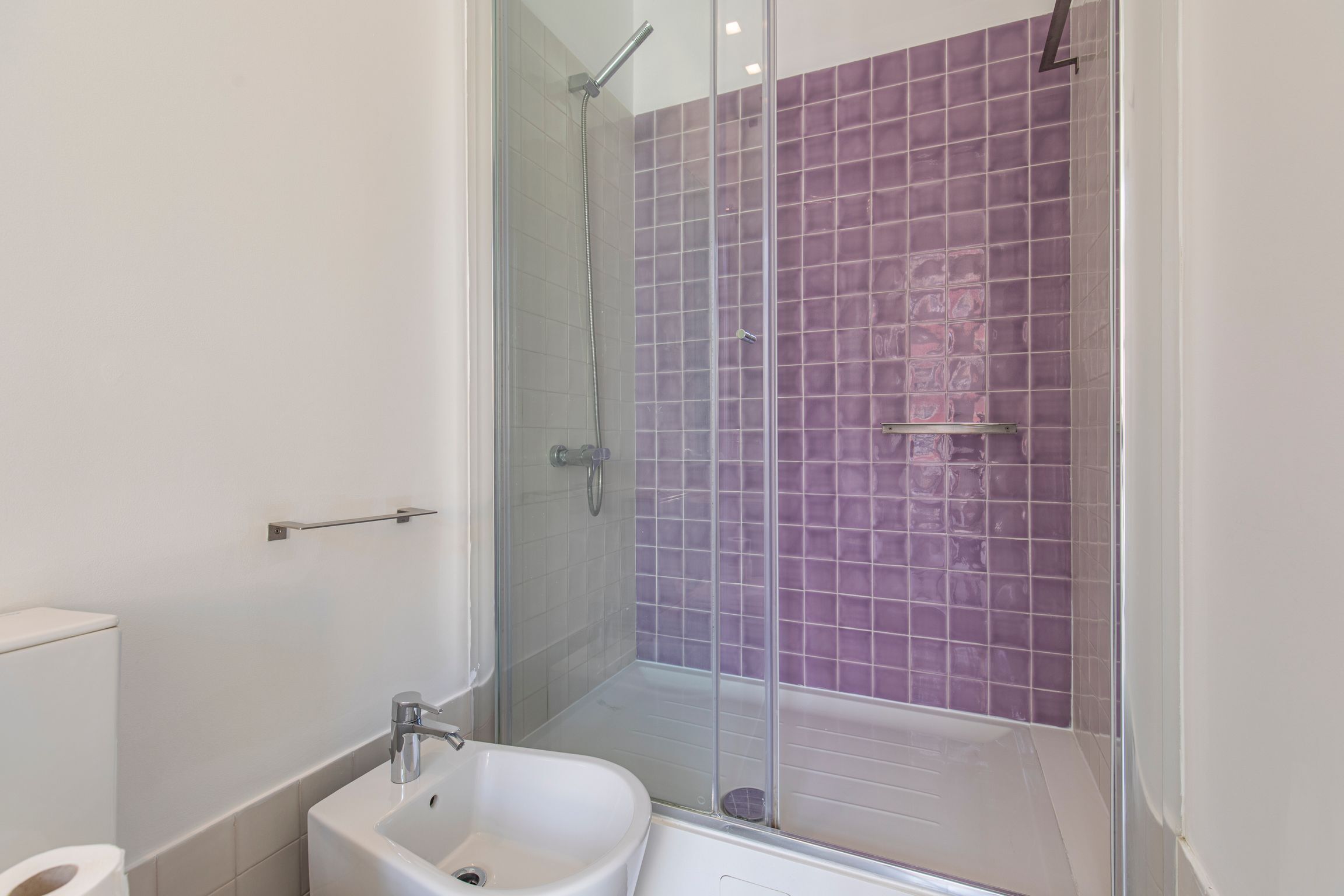 A bathroom with a glass-enclosed shower, a white sink, and a toilet.