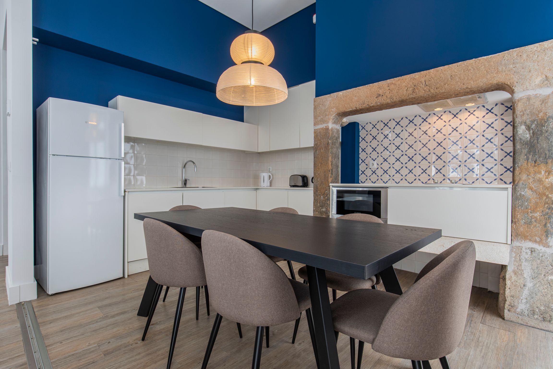 A modern kitchen with a dining area, featuring a large table and chairs, a refrigerator, and a stone accent wall.
