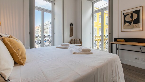 Een hotelkamer met een groot bed, twee ramen, een balkon en een schilderij aan de muur.