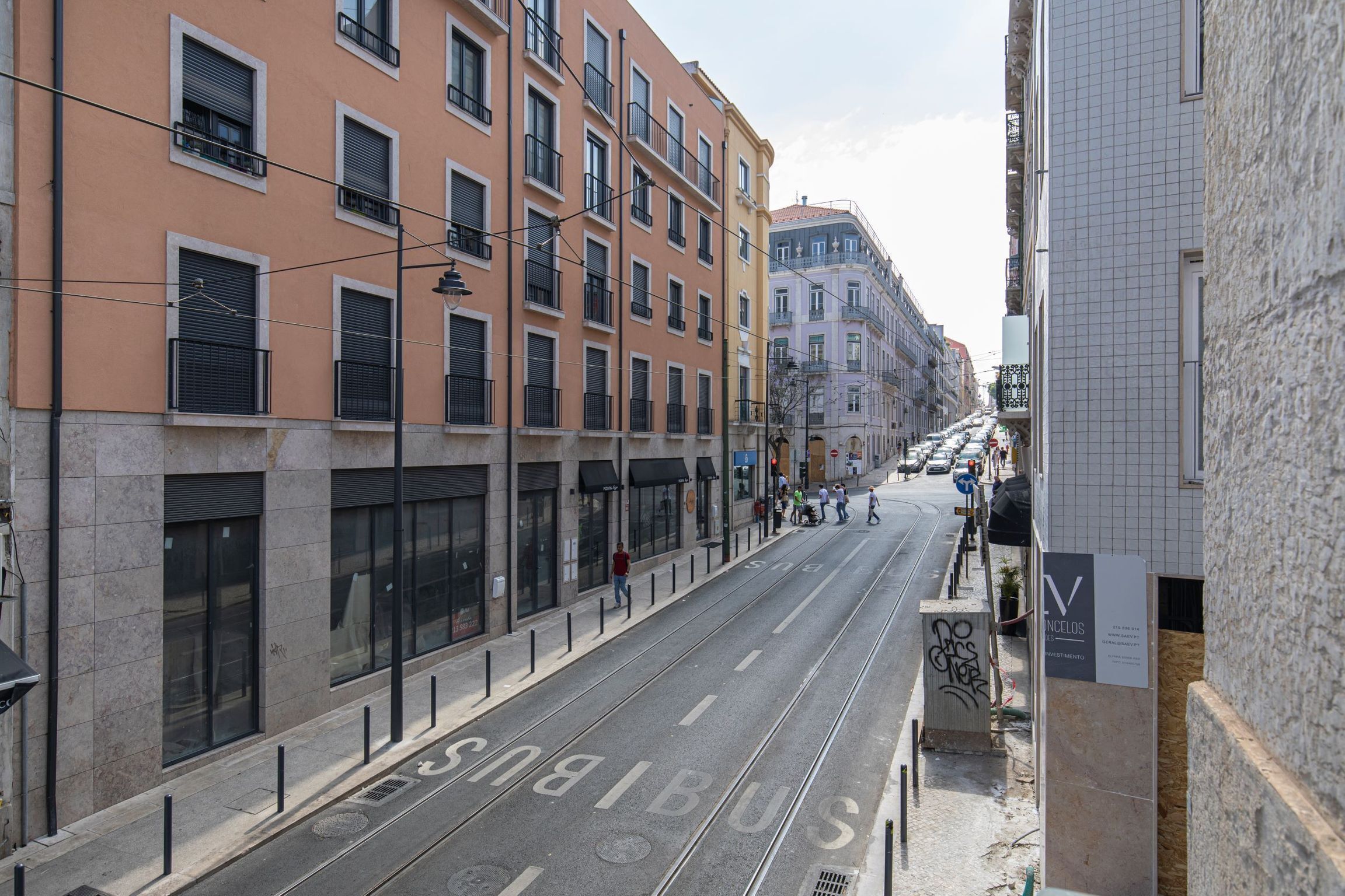 Una calle con edificios, una línea de tranvía y peatones.