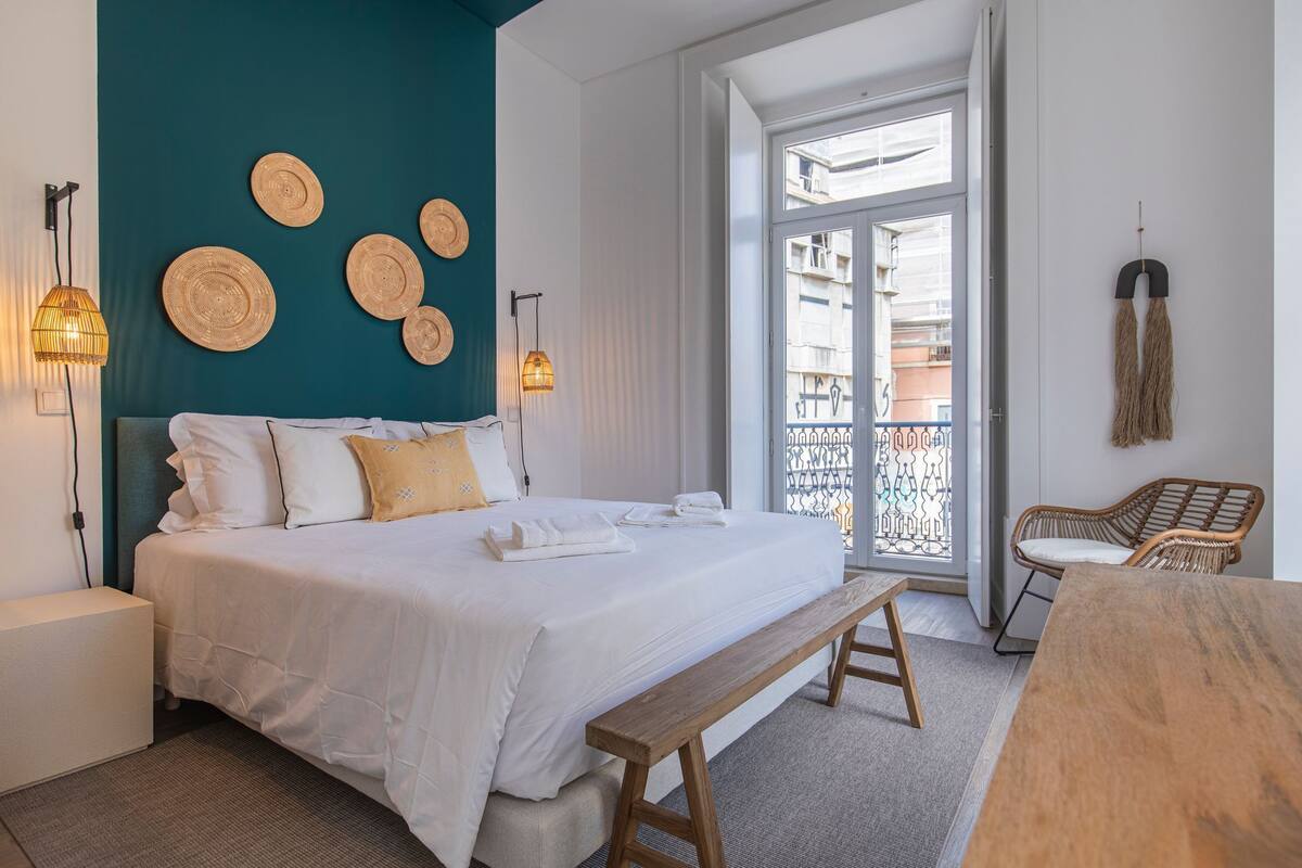 Un dormitorio con cama, lámparas de noche, un banco, una mesa de madera y vistas al balcón exterior.