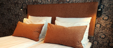 A bed with a patterned headboard, two pillows, and a wall with floral wallpaper.