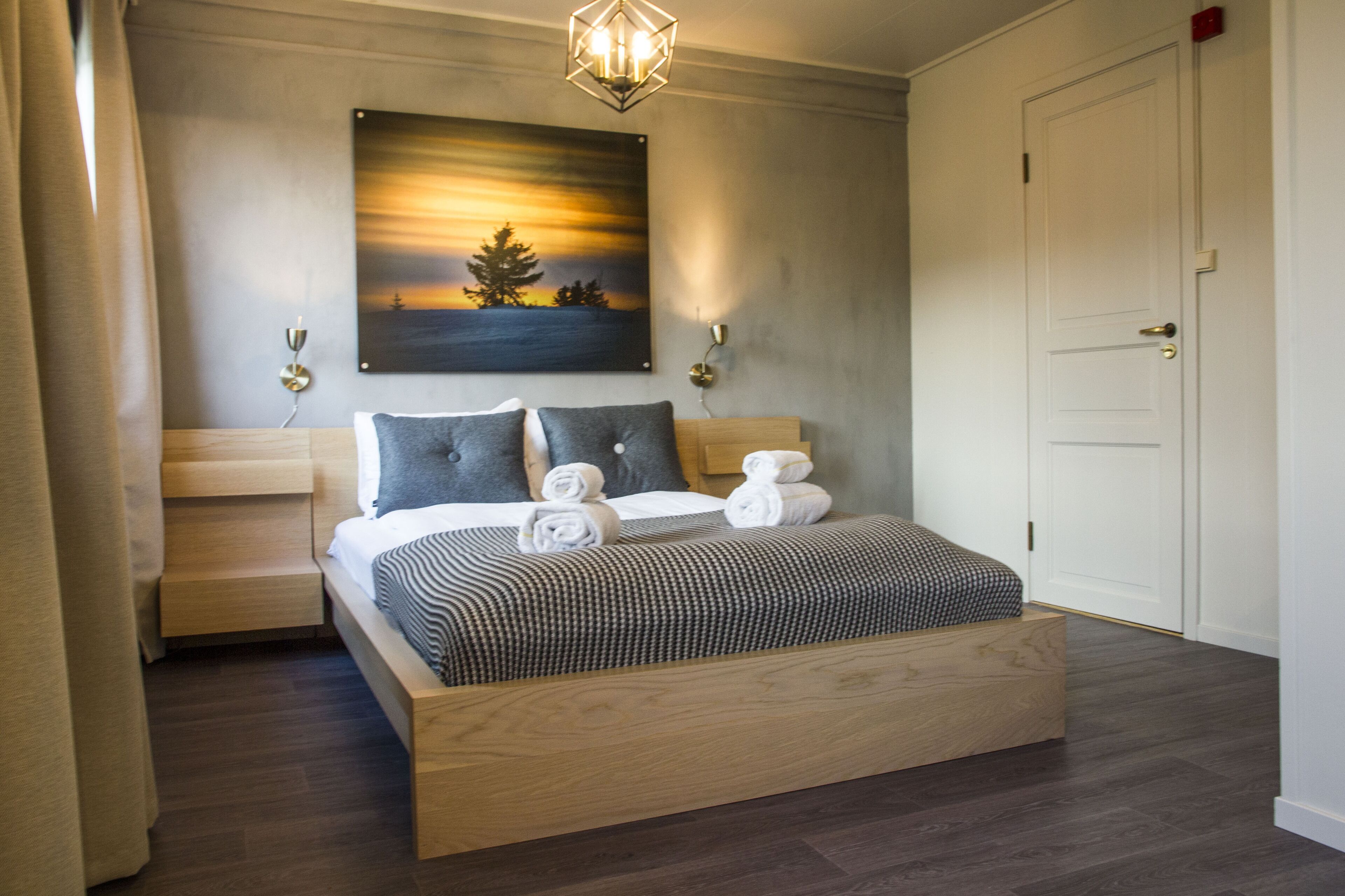 A modern bedroom with a wooden bed, a painting of a sunset, and a door.