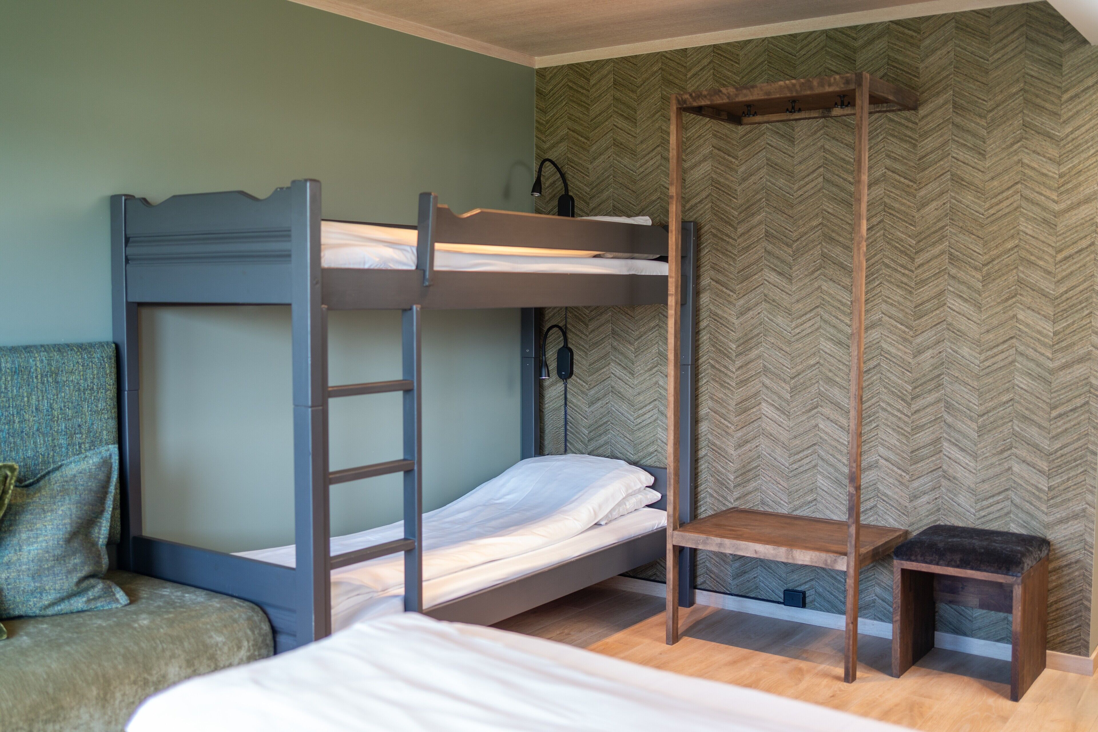 A bunk bed room with a wooden ladder, a small wooden bench, and a green upholstered chair.