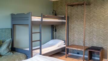 A bunk bed room with a wooden ladder, a small wooden bench, and a green upholstered chair.