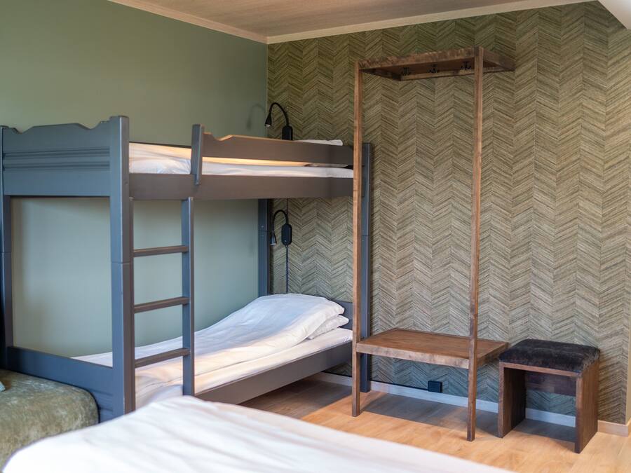 A bunk bed room with a wooden ladder, a small wooden bench, and a green upholstered chair.