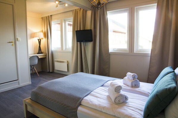 A hotel room with a bed, a desk with a lamp, a TV, and a view of the outside through the windows. - Lillehammer Turistsenter Budget Hotel (Lillehammer)