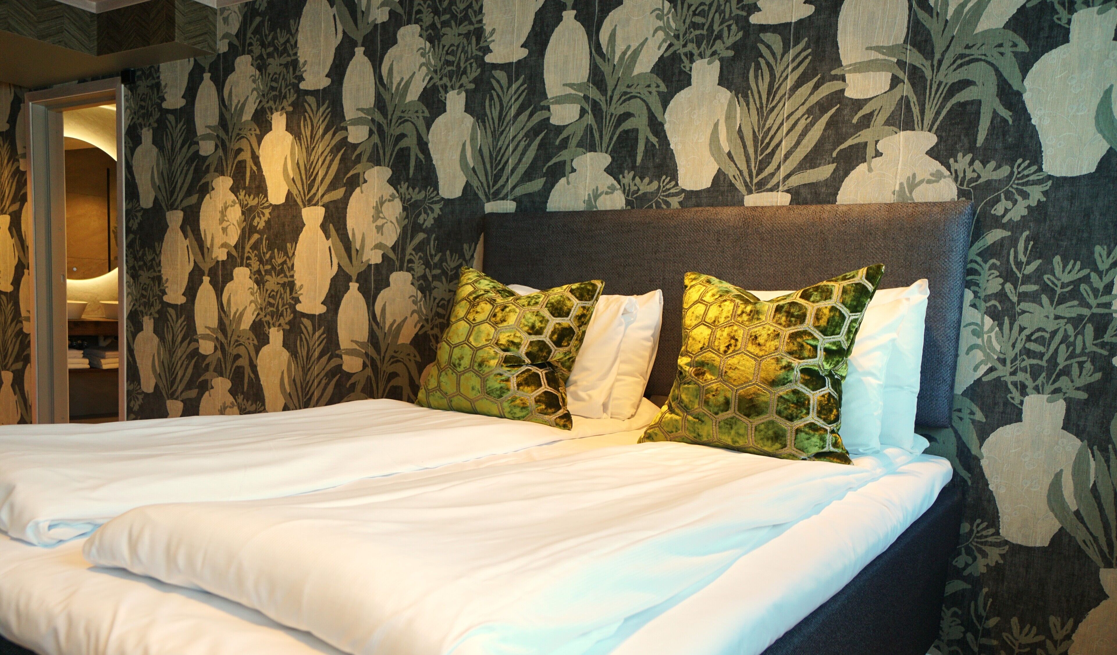 A neatly made bed with white linens, a dark headboard, and decorative pillows with a honeycomb pattern.
