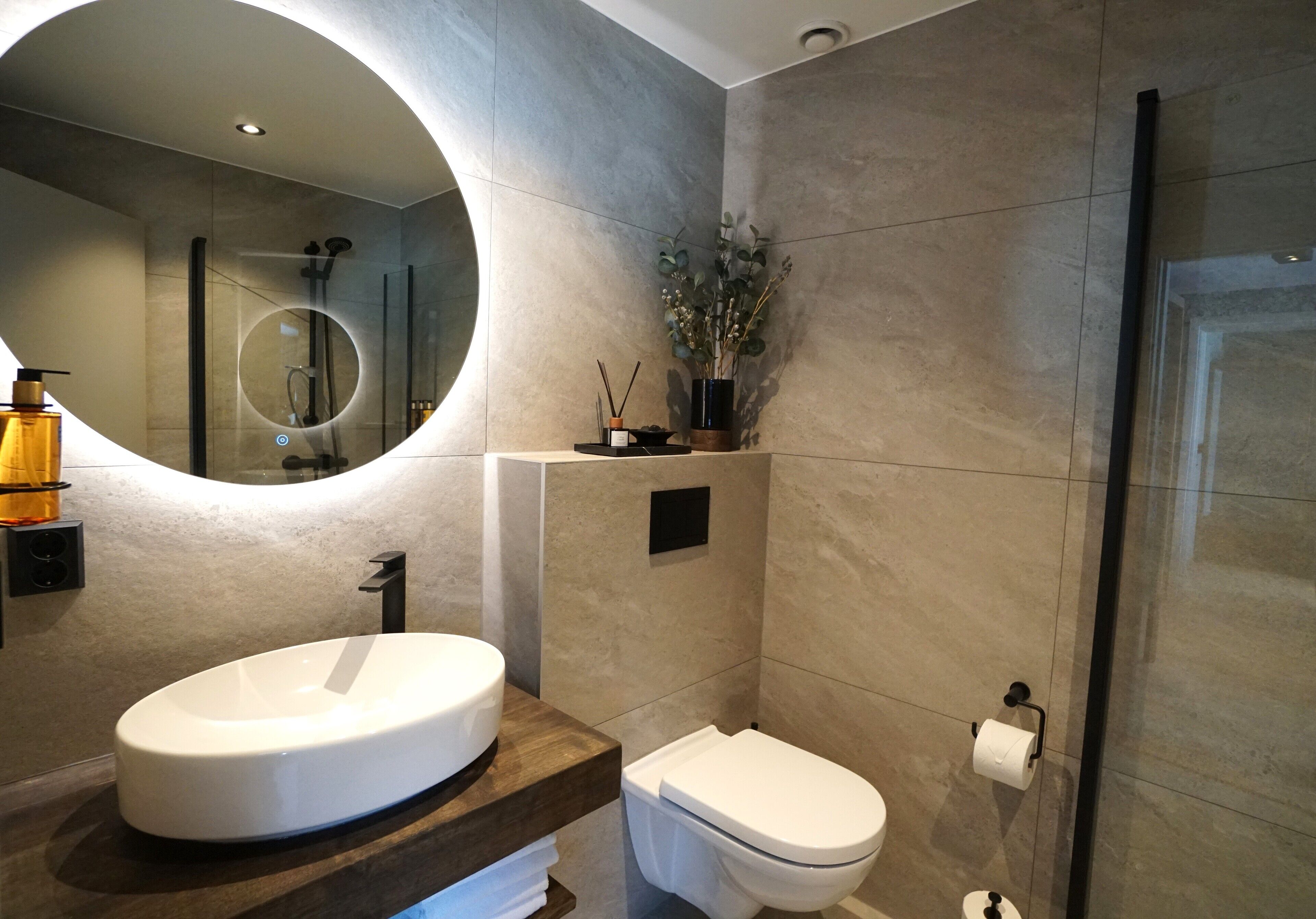 A modern bathroom with a round mirror, a white sink, and a toilet.