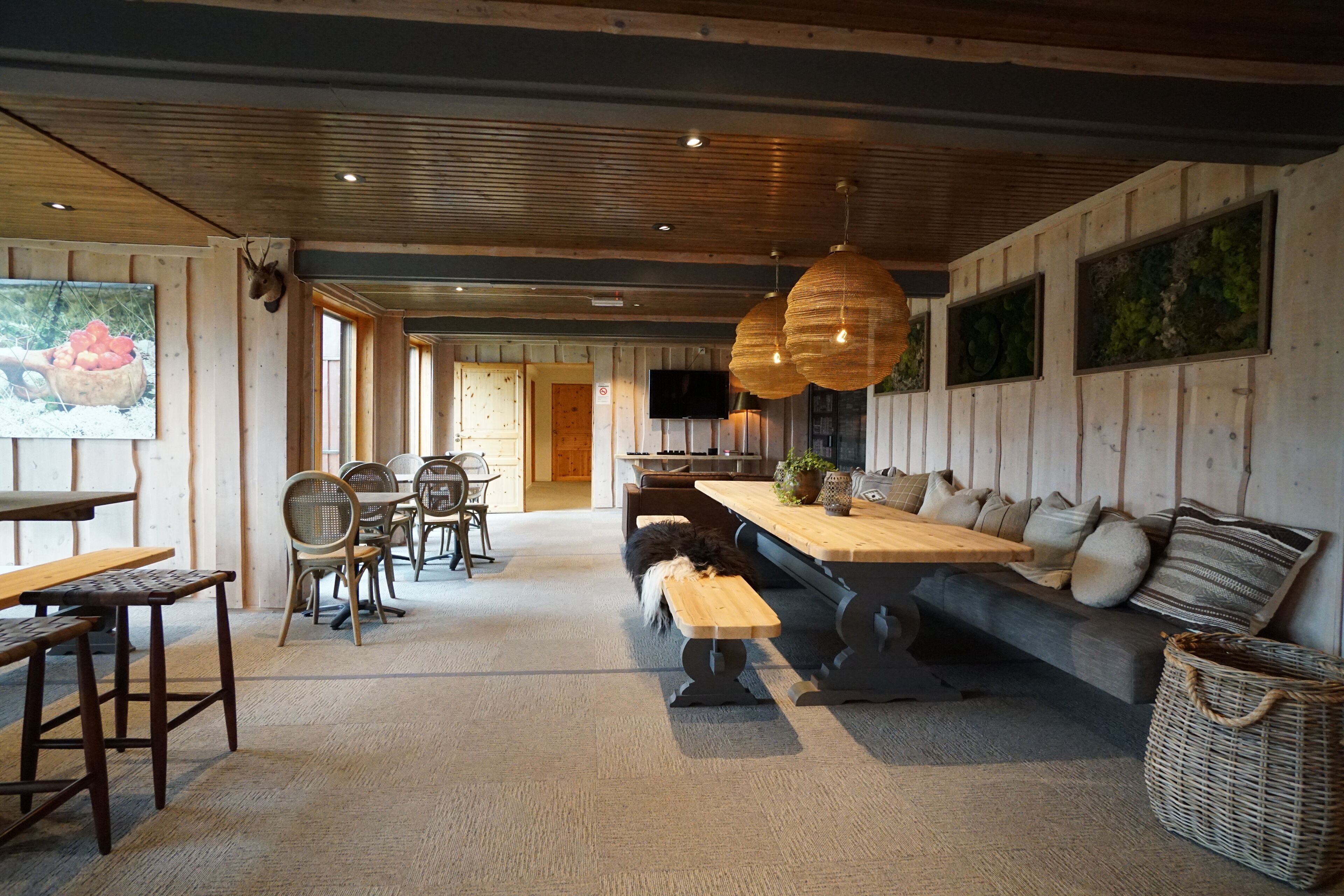 Un coin repas chaleureux avec des tables et des bancs en bois, un canapé avec des coussins et des lanternes suspendues.