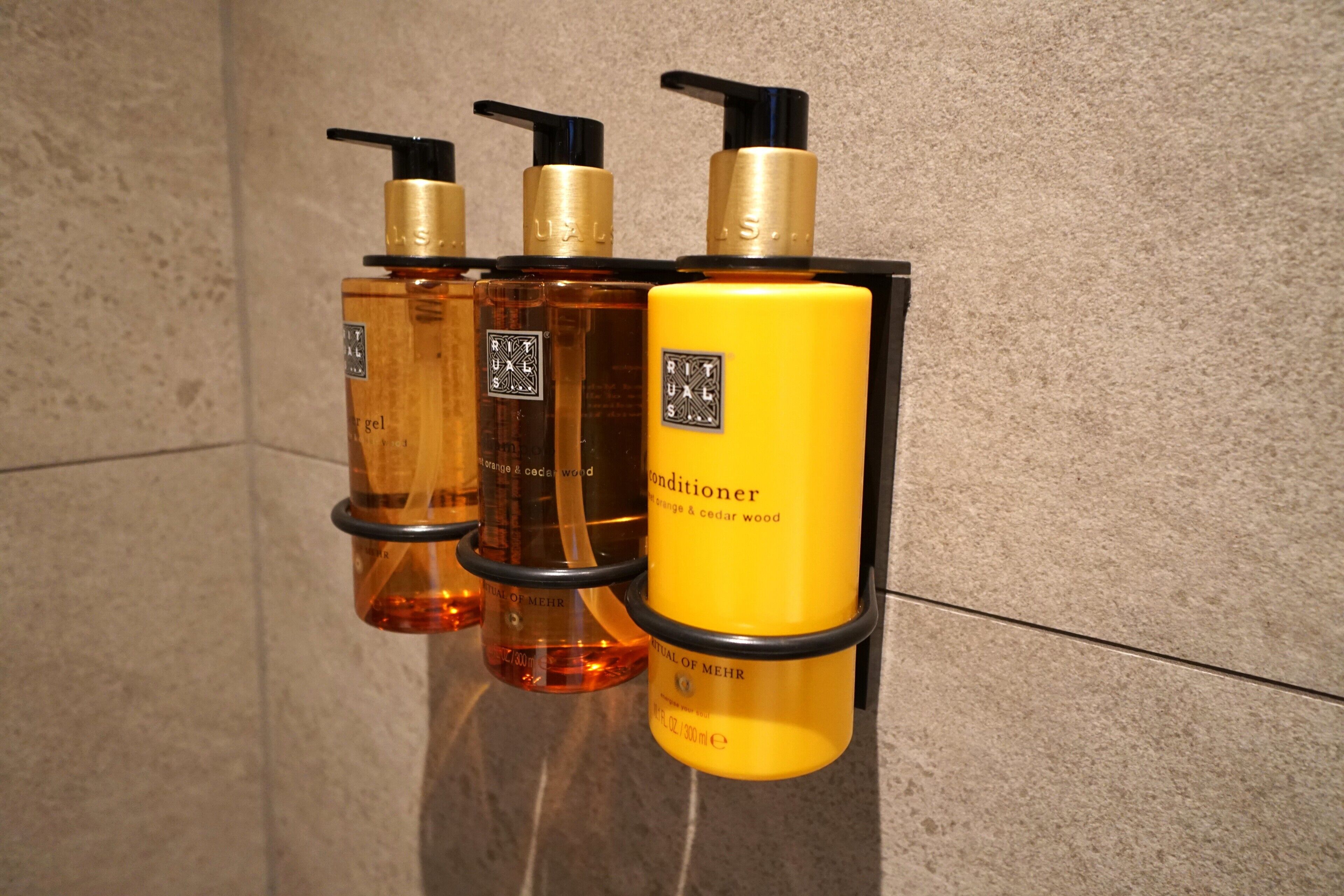 Three bottles of conditioner with black pumps and a yellow label, arranged on a tiled surface.