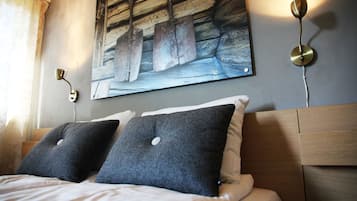 Una cama bien hecha con dos almohadas, un cuadro en la pared y una lámpara fijada a la pared.