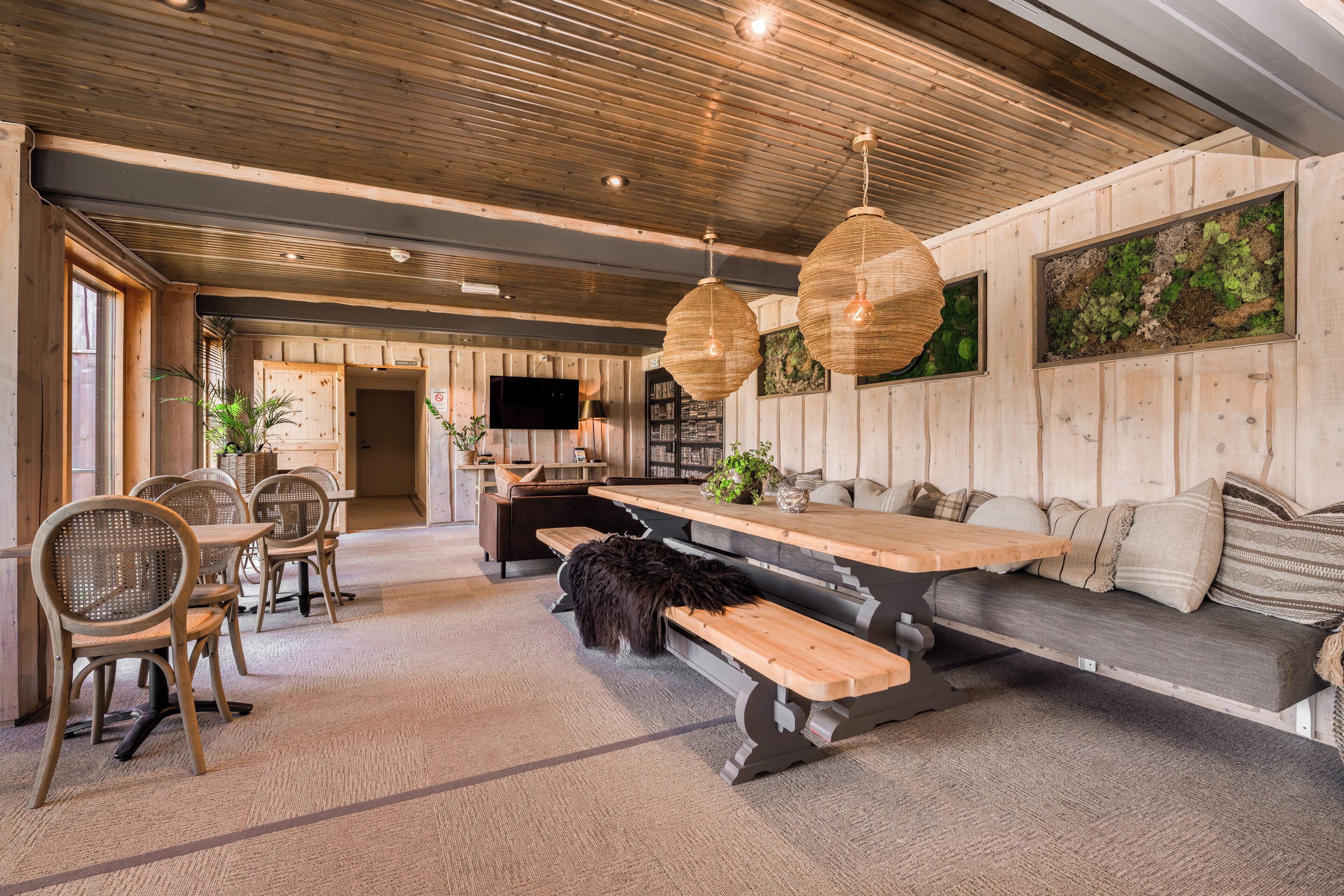 Un interior acogedor con techo de madera, un banco largo y una zona de comedor con sillas y mesa.