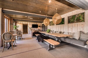 Un interior acogedor con techo de madera, un banco largo y una zona de comedor con sillas y mesa.