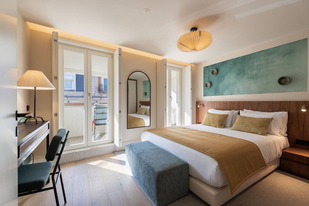 Une chambre d’hôtel moderne dotée d’un grand lit, d’un bureau avec une chaise, d’un balcon avec des portes vitrées et d’une vue sur la ville.