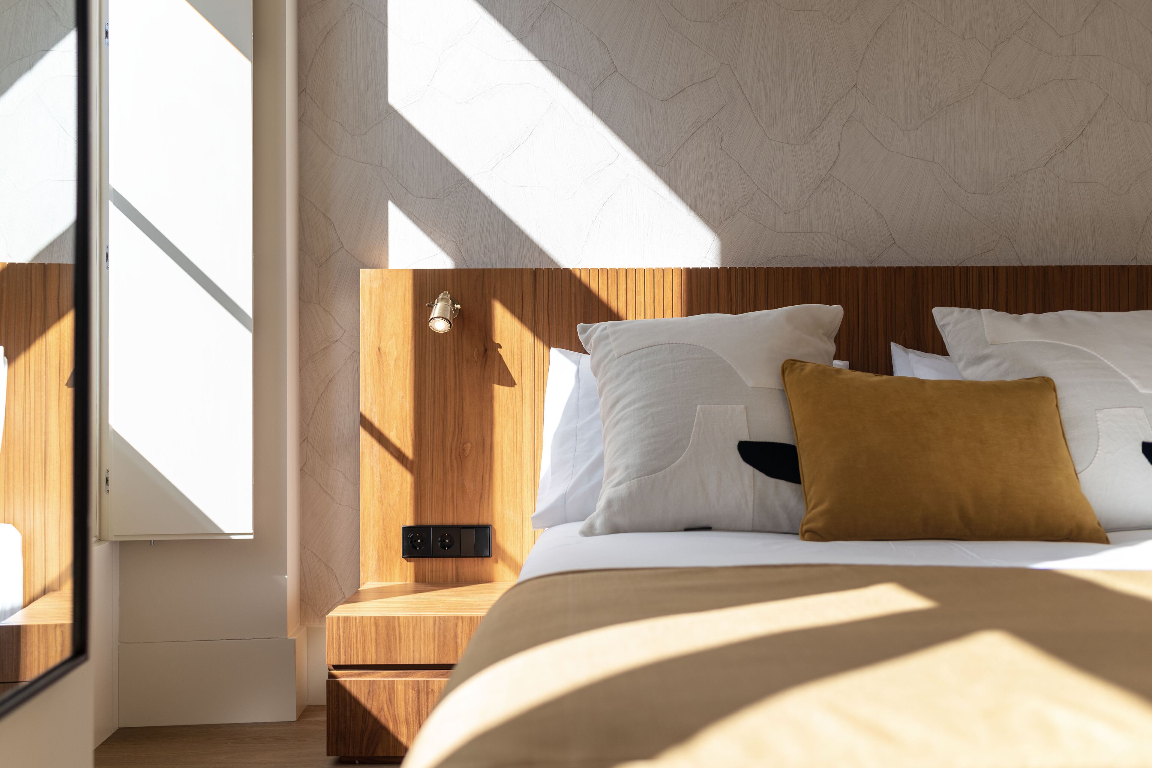 A bedroom with a wooden headboard, white bedding, and a brown accent pillow.