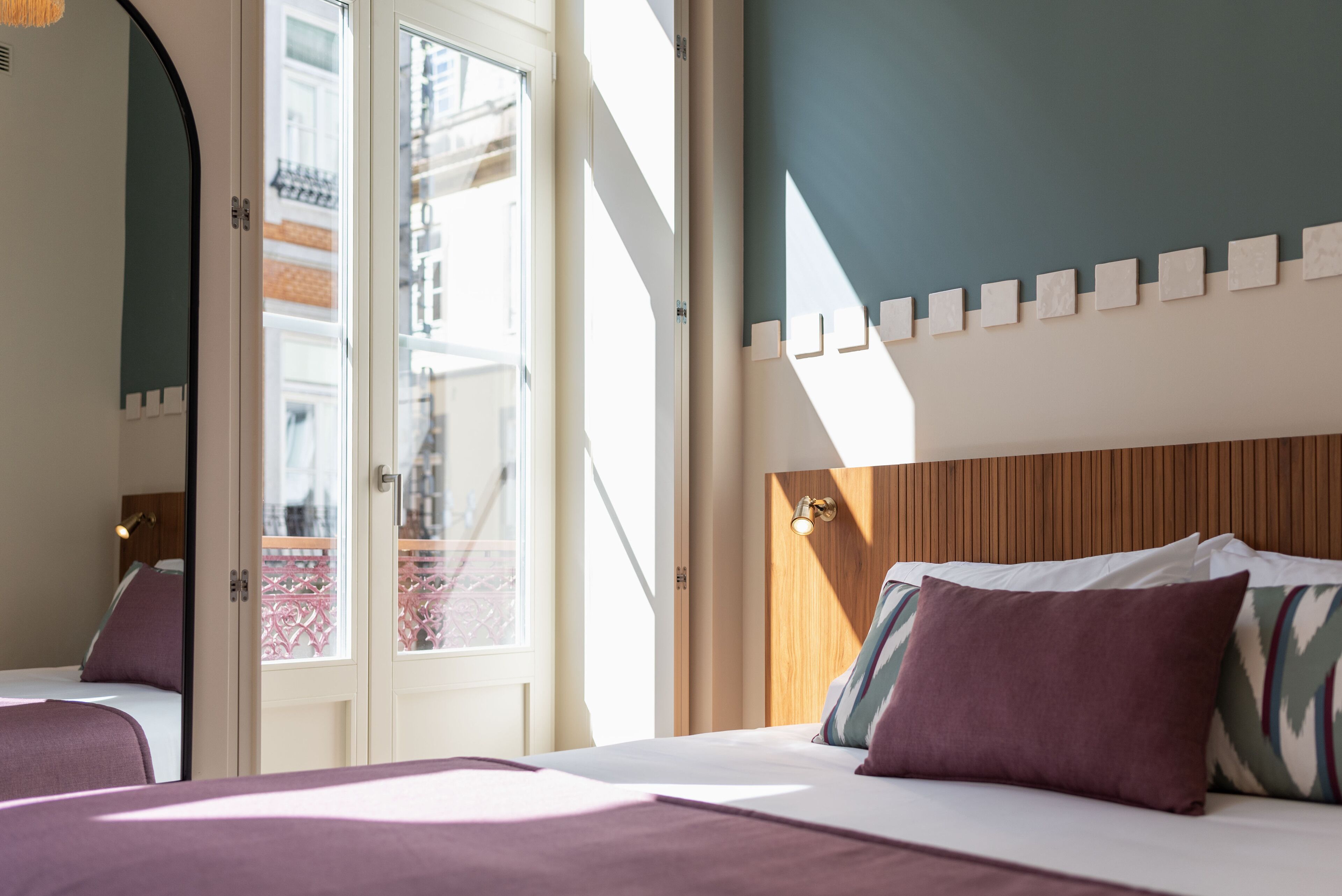 A hotel room with a bed, a wooden headboard, and a view of buildings through a glass door.