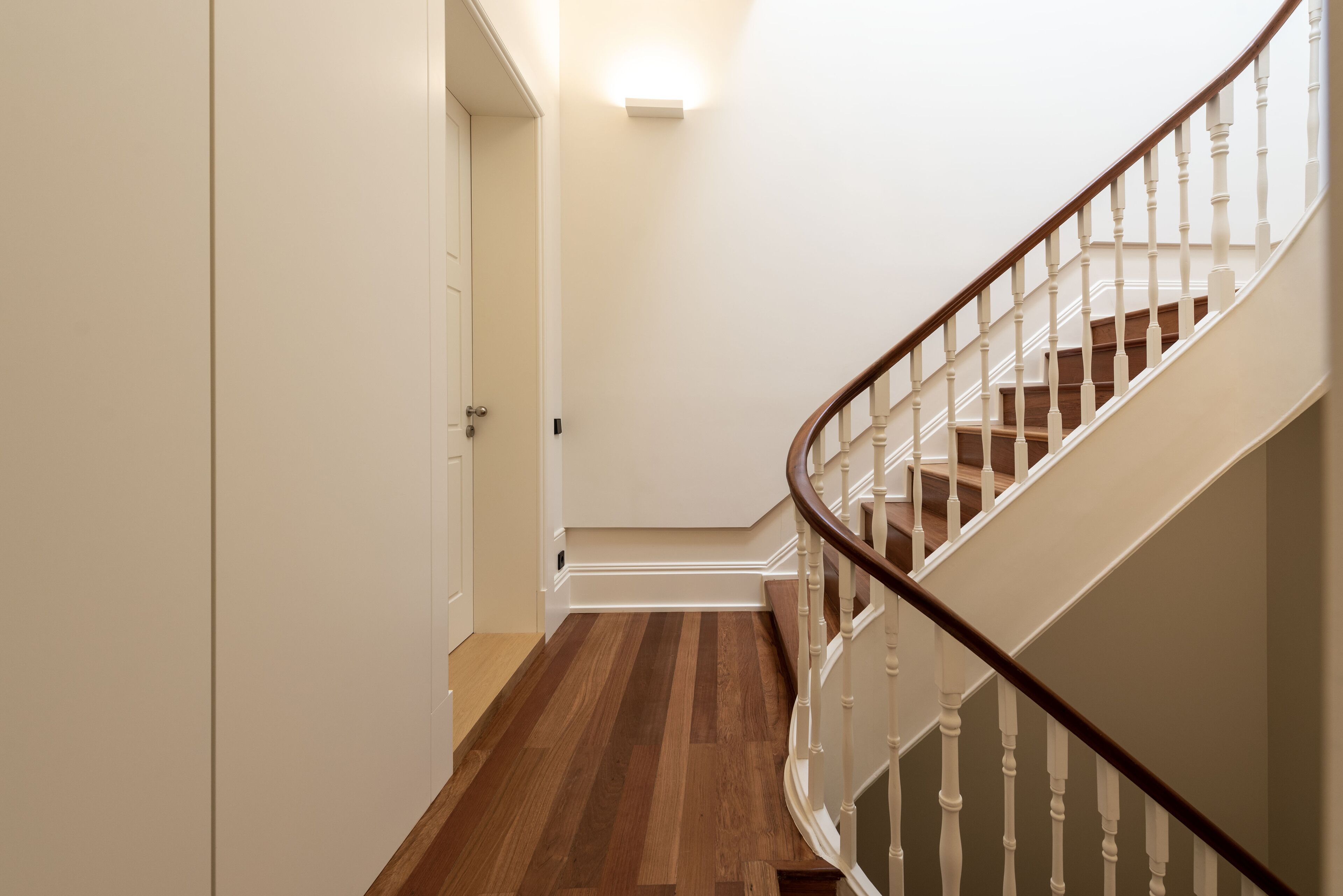 Un escalier avec des marches en bois et des balustrades blanches, menant à un palier où se trouve un luminaire.