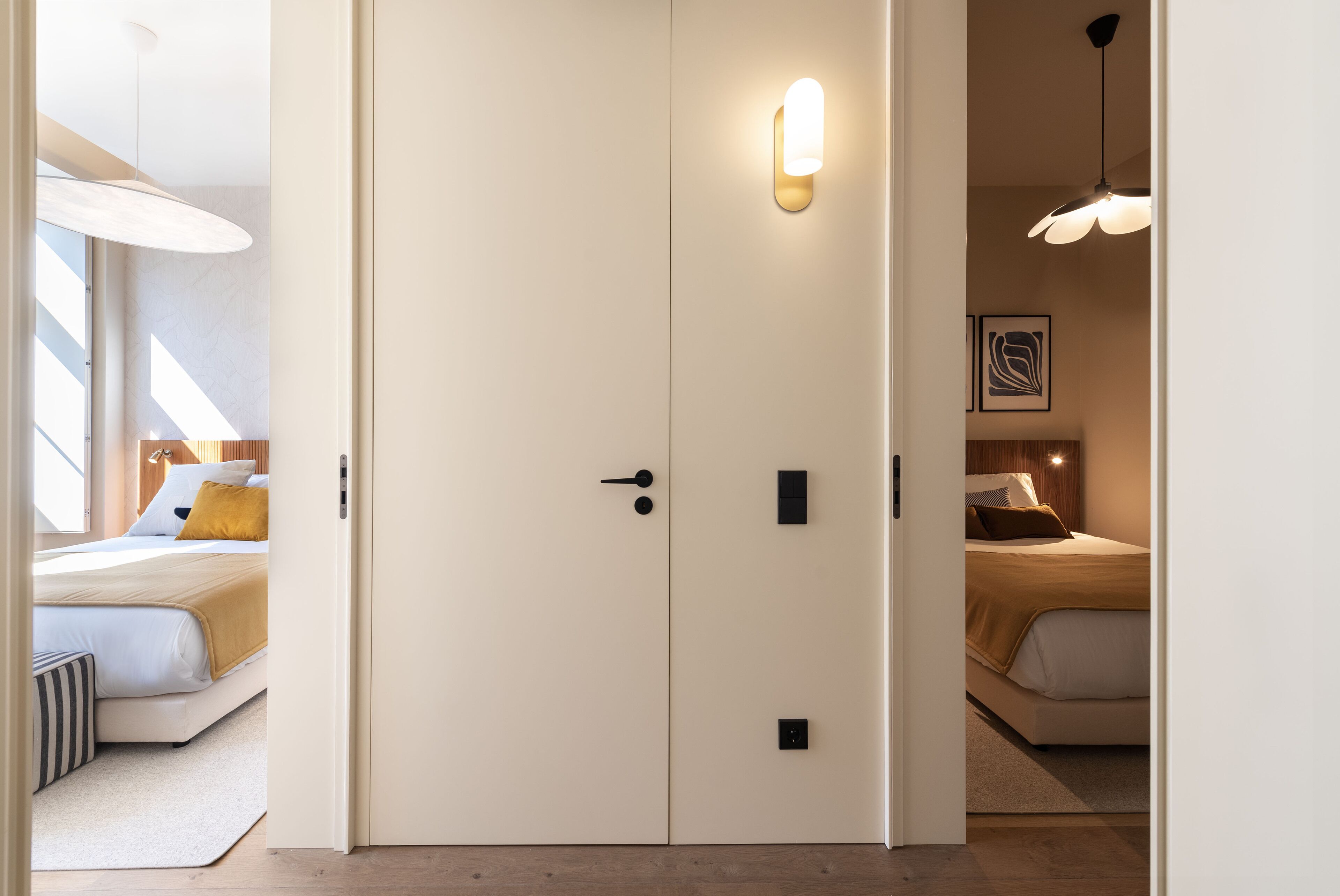 Hotelkamer met een dubbele deur, een bed met een geel kussen, een nachtkastje en een wandlamp.