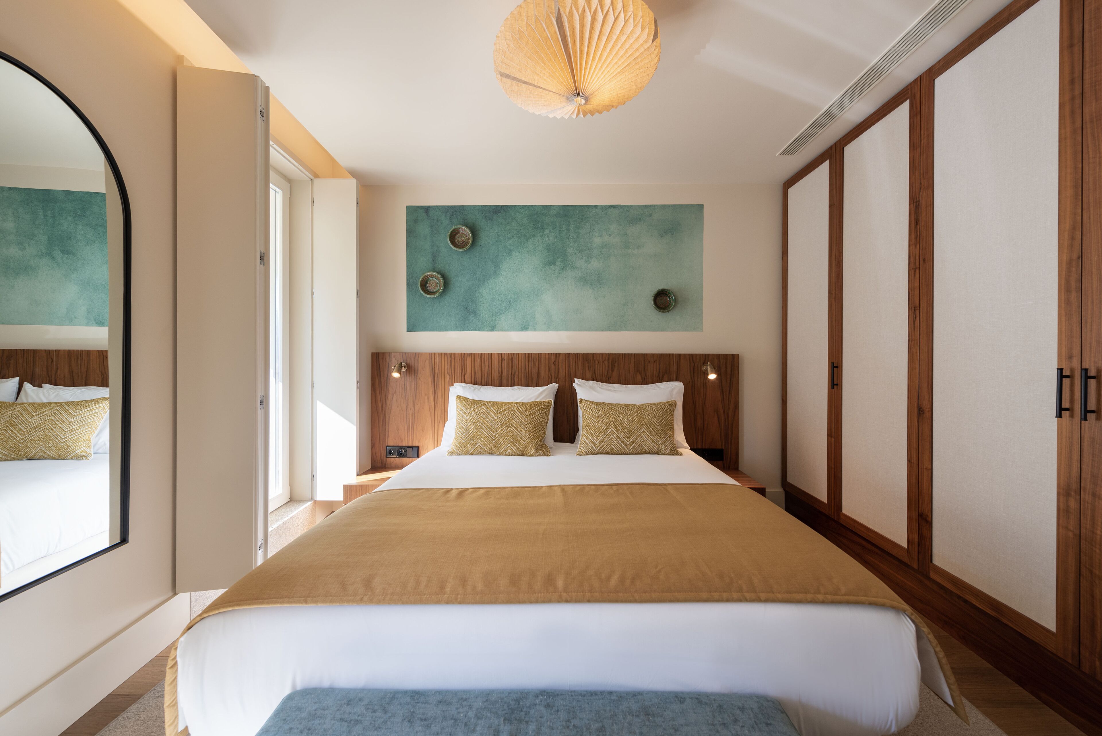 A large bed with a wooden headboard, a mirror, and a wall-mounted artwork.