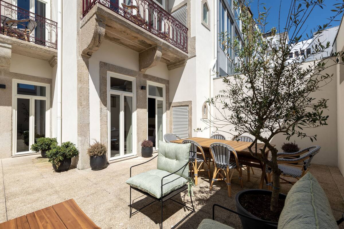 Une cour avec une table et des chaises en bois, des plantes en pot et un petit arbre.