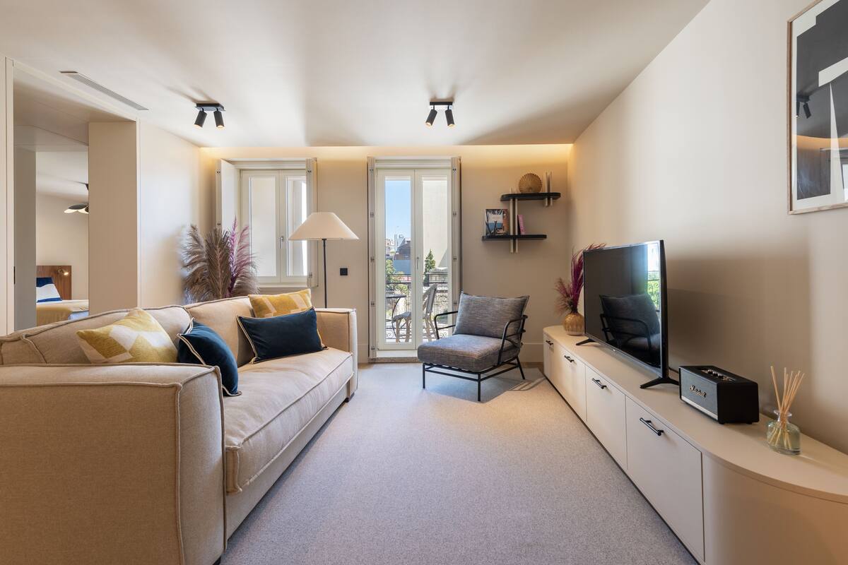 Un salon moderne avec un canapé, un fauteuil, une télévision et une vue sur le balcon.