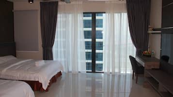 A hotel room with a bed, a desk, and a view of the city through large windows.