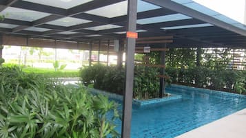 A covered swimming pool with a glass ceiling, surrounded by lush greenery.