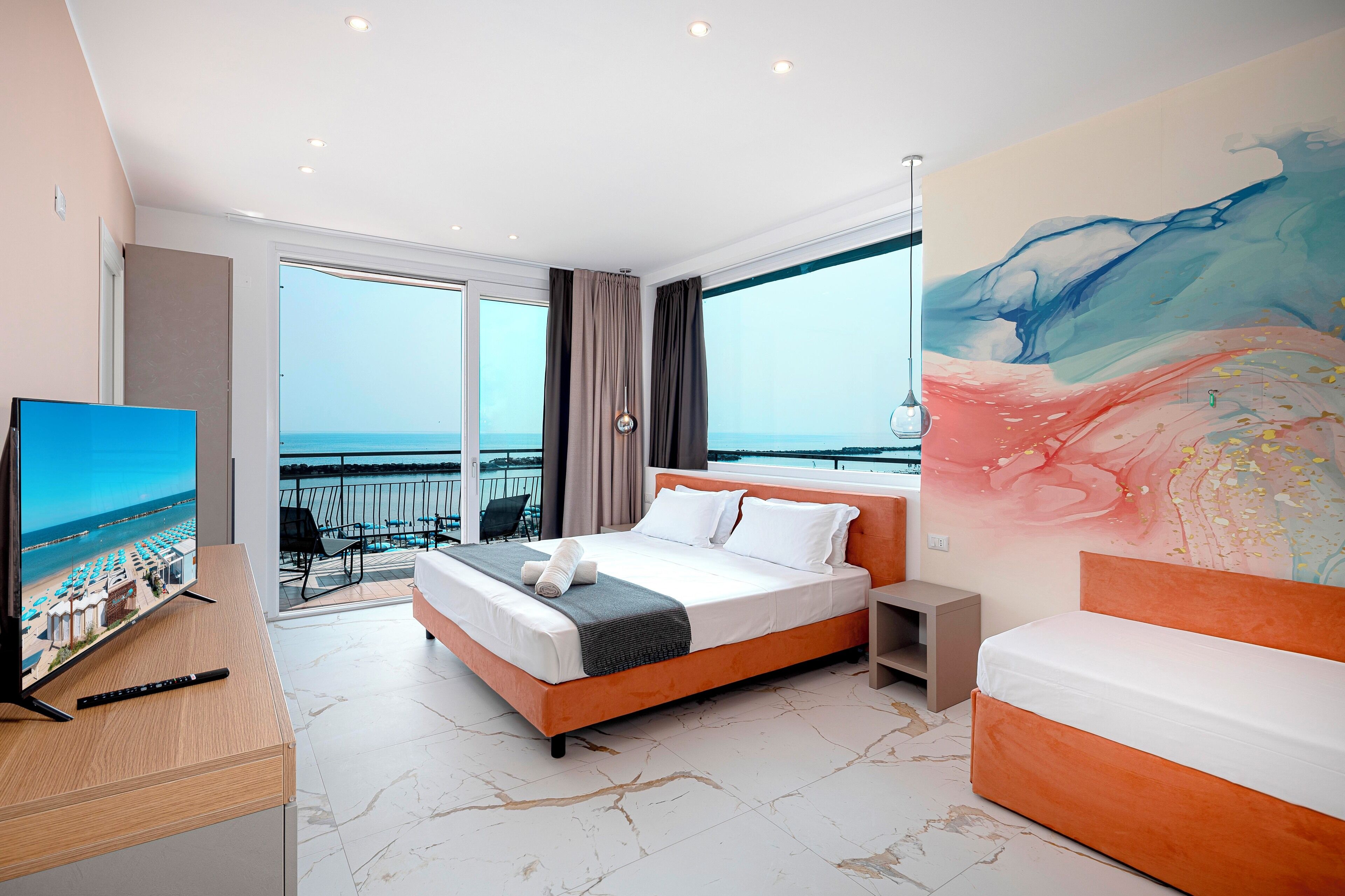 Una habitación de hotel con una cama grande, televisión y balcón con vista al mar.