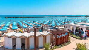 Ein Strandhotel mit zahlreichen blauen Sonnenschirmen, Strandhütten und einem Restaurantbereich.