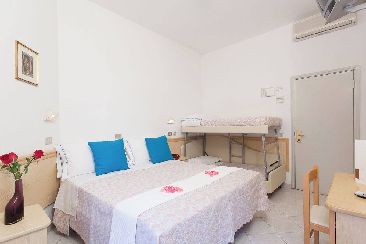 Un dormitorio con una litera, una mesita de noche con un florero y un escritorio con una silla.
