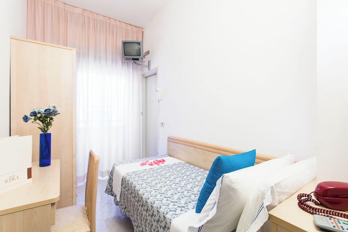 Habitación de hotel con cama, escritorio, teléfono, televisión y ventana con cortinas.