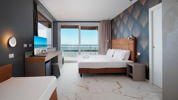 Ein Hotelzimmer mit Bett, Schreibtisch, Fernseher und einem Balkon mit Meerblick.