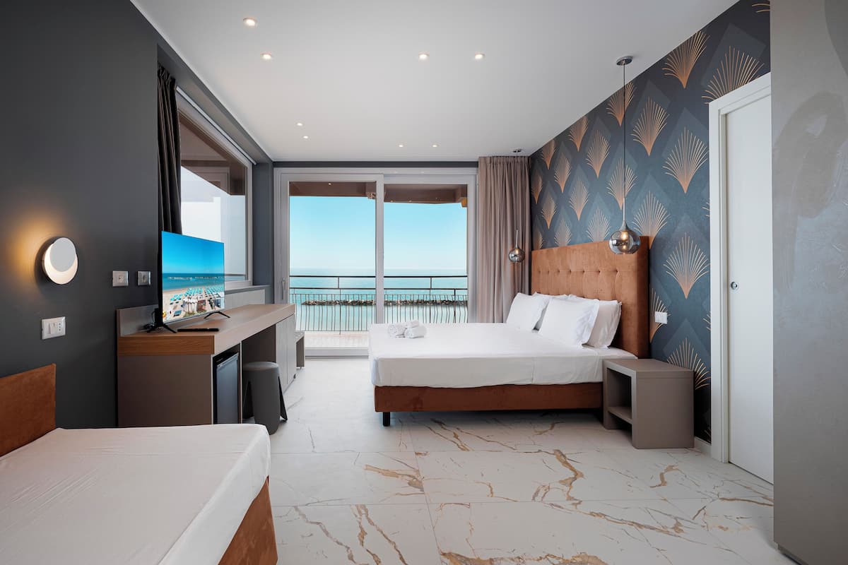 Habitación de hotel con cama, escritorio, televisión y balcón con vista al mar.