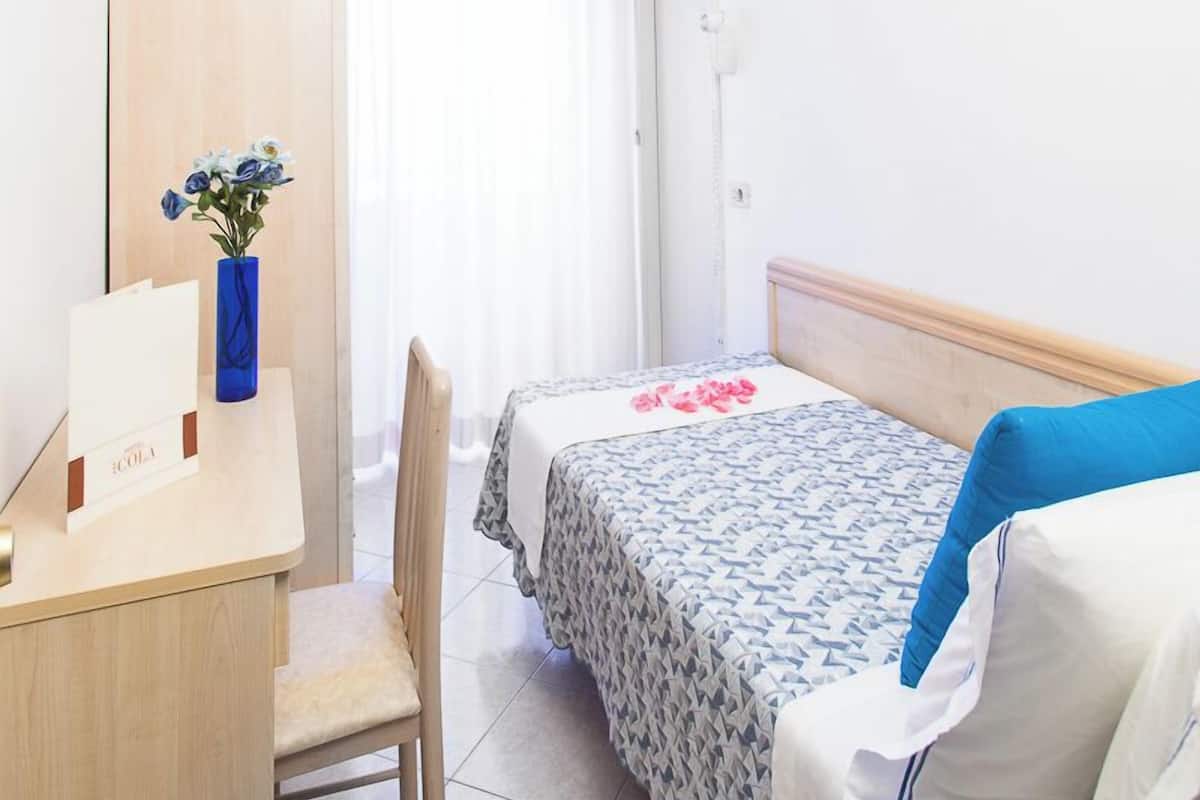 Una habitación pequeña y limpia con cama, escritorio, silla, televisor y ventana con cortinas.
