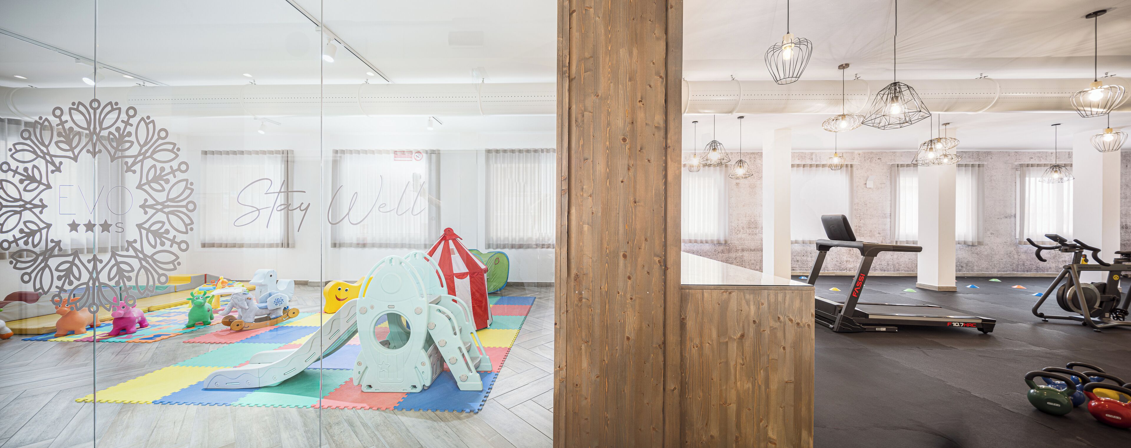 Un espace intérieur moderne comprenant un espace de jeux pour enfants, du matériel d’exercice et une grande colonne en bois.