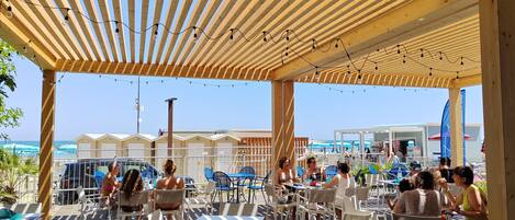 Eine Außenpatio mit Tischen und Stühlen, einer Holzpergola und Lichterketten.