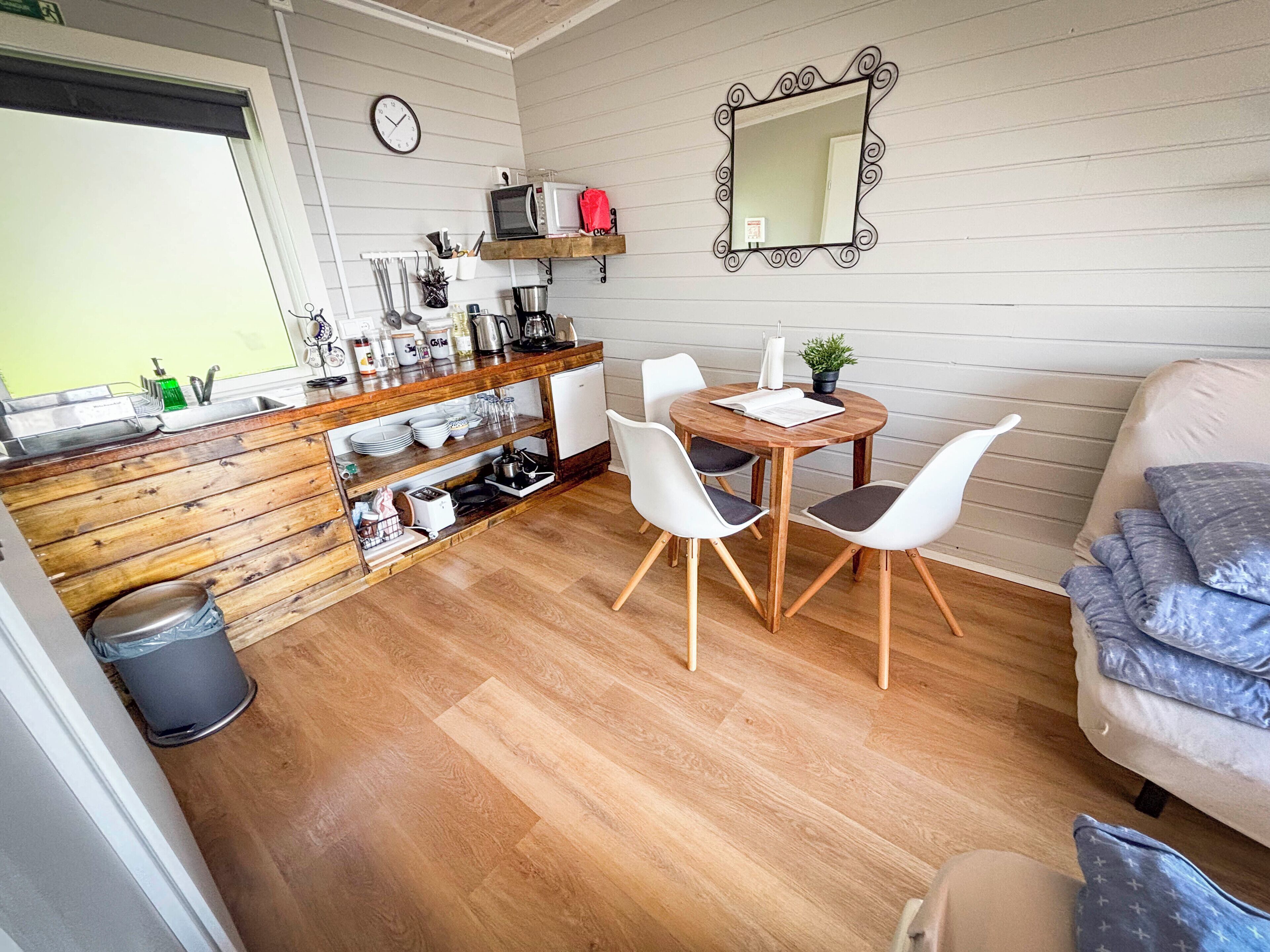 A compact kitchen with wooden cabinetry, a dining table with chairs, a mirror, and a clock on the wall.