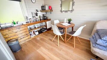 A compact kitchen with wooden cabinetry, a dining table with chairs, a mirror, and a clock on the wall.
