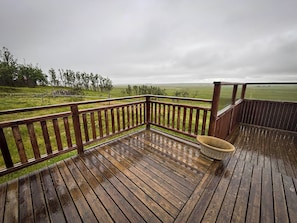 A wooden deck with a view of a grassy field and trees. - Áshamrar (Selfoss)